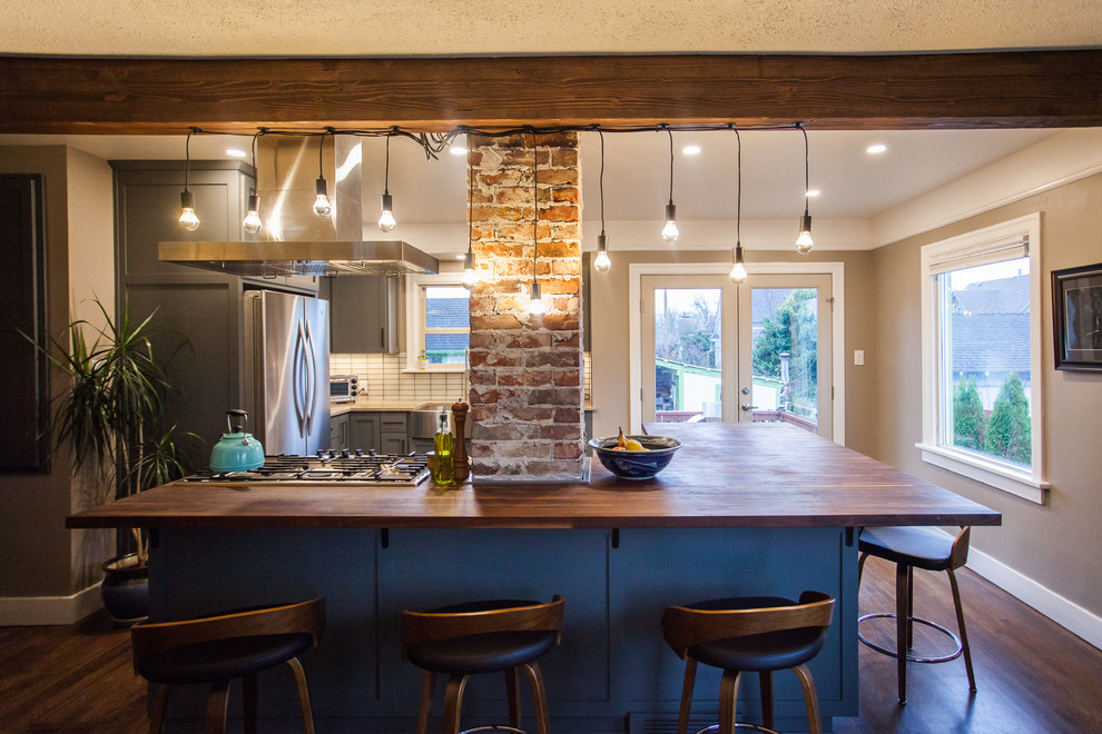 Inspiration for a small transitional l-shaped dark wood floor and brown floor open concept kitchen remodel in Seattle with a farmhouse sink, shaker cabinets, gray cabinets, stainless steel appliances, an island, granite countertops, white backsplash, porcelain backsplash and beige countertops