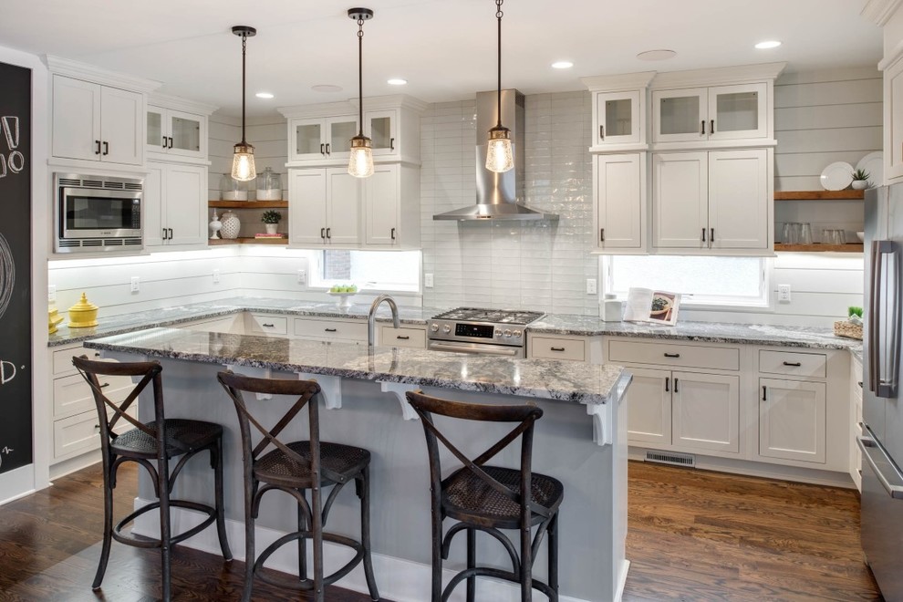 Photo of a large transitional u-shaped eat-in kitchen in Minneapolis with a single-bowl sink, shaker cabinets, white cabinets, quartz benchtops, white splashback, glass tile splashback, stainless steel appliances, medium hardwood floors and with island.