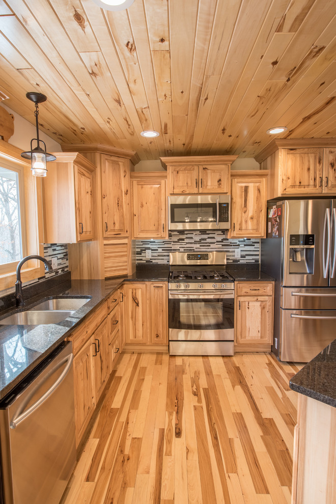 Example of a mid-sized mountain style l-shaped light wood floor open concept kitchen design in Minneapolis with a double-bowl sink, raised-panel cabinets, light wood cabinets, granite countertops, multicolored backsplash, matchstick tile backsplash, stainless steel appliances and an island