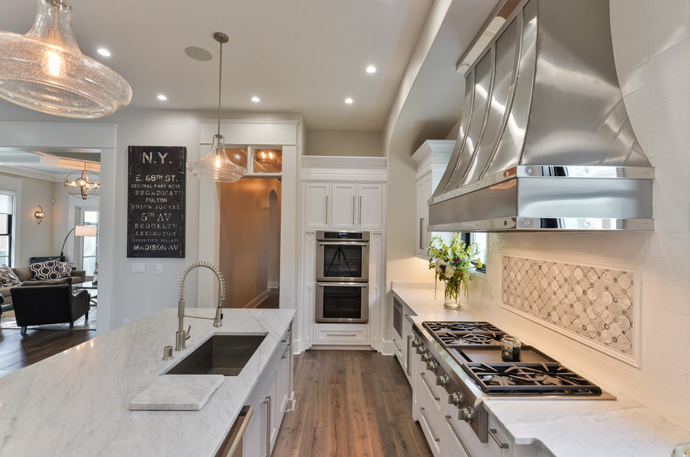 Transitional galley open plan kitchen in Louisville with an undermount sink, shaker cabinets, white cabinets, marble benchtops, white splashback, subway tile splashback, stainless steel appliances, medium hardwood floors and with island.