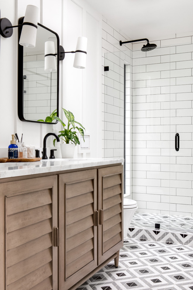 This is an example of a beach style bathroom in Orange County with louvered cabinets, medium wood cabinets, an alcove shower, white tile, subway tile, white walls, an undermount sink, multi-coloured floor, a hinged shower door, white benchtops, a double vanity, a freestanding vanity and panelled walls.