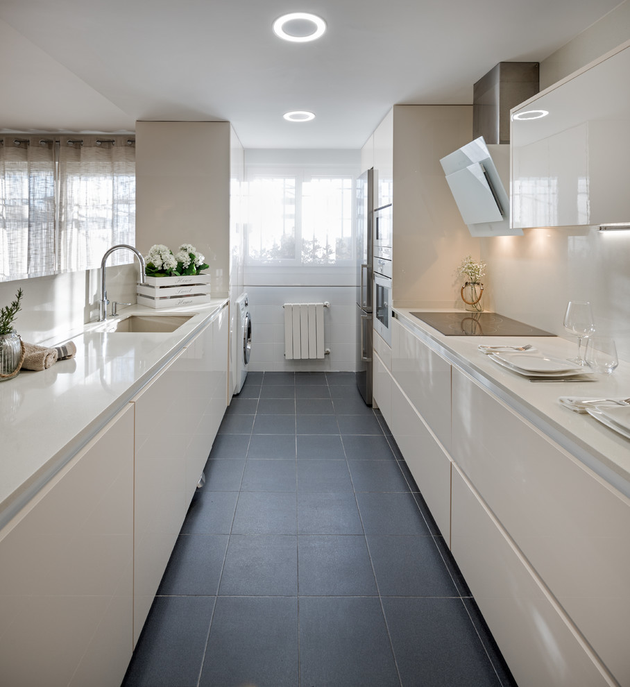 Photo of a mid-sized contemporary galley separate kitchen in Madrid with flat-panel cabinets, white cabinets, quartz benchtops, white splashback, stainless steel appliances, ceramic floors, no island, black floor and an undermount sink.