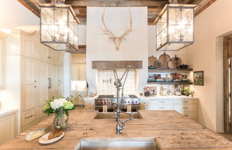 Huge farmhouse medium tone wood floor and brown floor eat-in kitchen photo in Austin with a farmhouse sink, shaker cabinets, beige cabinets, wood countertops, brown countertops, white backsplash, terra-cotta backsplash, paneled appliances and an island