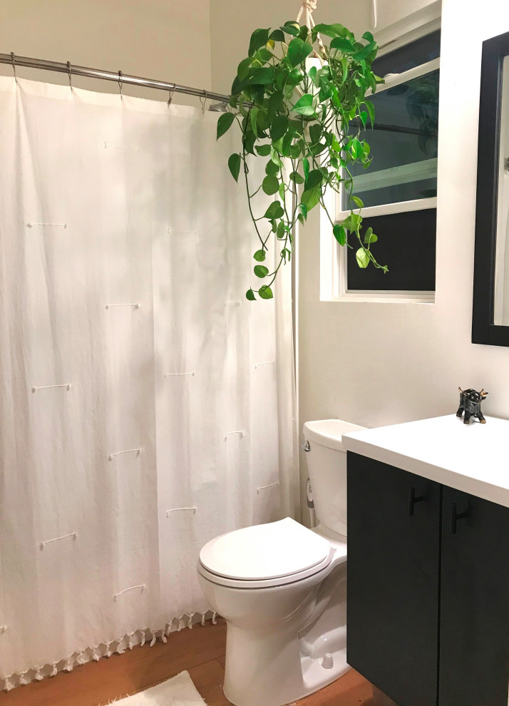 Inspiration for a small modern master bathroom in San Diego with flat-panel cabinets, black cabinets, an alcove tub, a shower/bathtub combo, a two-piece toilet, white tile, white walls, vinyl floors, an integrated sink, solid surface benchtops, yellow floor, a shower curtain, white benchtops, a single vanity and a floating vanity.
