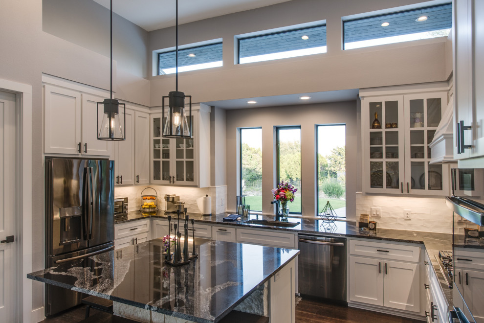 Inspiration for a large contemporary u-shaped dark wood floor and vaulted ceiling open concept kitchen remodel in Austin with a drop-in sink, beaded inset cabinets, white cabinets, quartz countertops, white backsplash, stone tile backsplash, stainless steel appliances, an island and black countertops