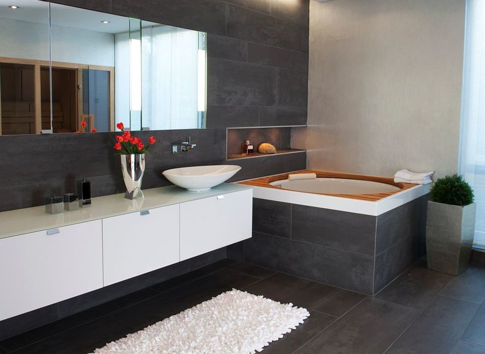 Inspiration for a large contemporary master bathroom in Nuremberg with a vessel sink, flat-panel cabinets, white cabinets, a japanese tub, gray tile, grey walls, stone slab, slate floors and glass benchtops.