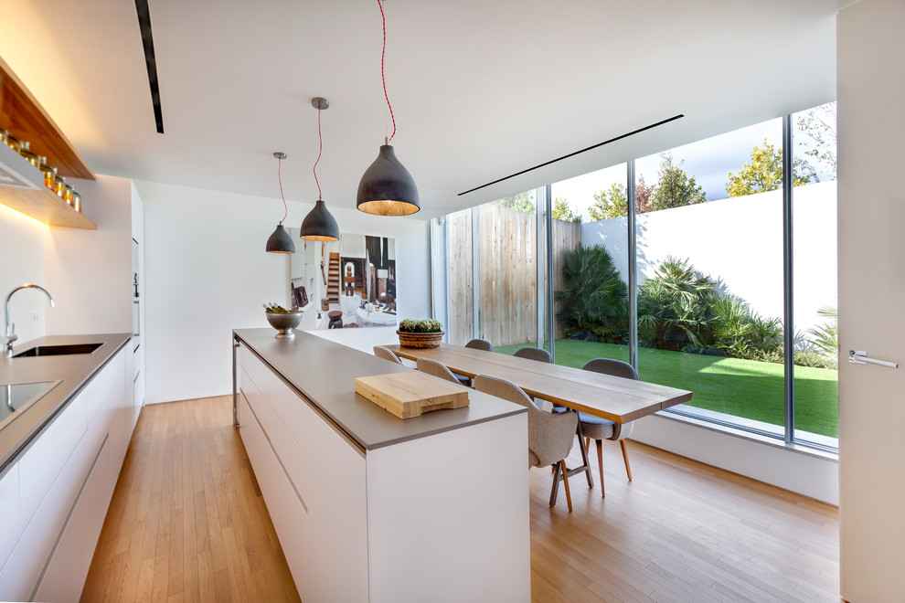 Photo of a mid-sized contemporary galley eat-in kitchen in Other with a drop-in sink, flat-panel cabinets, white cabinets, white splashback, stainless steel appliances, medium hardwood floors and with island.