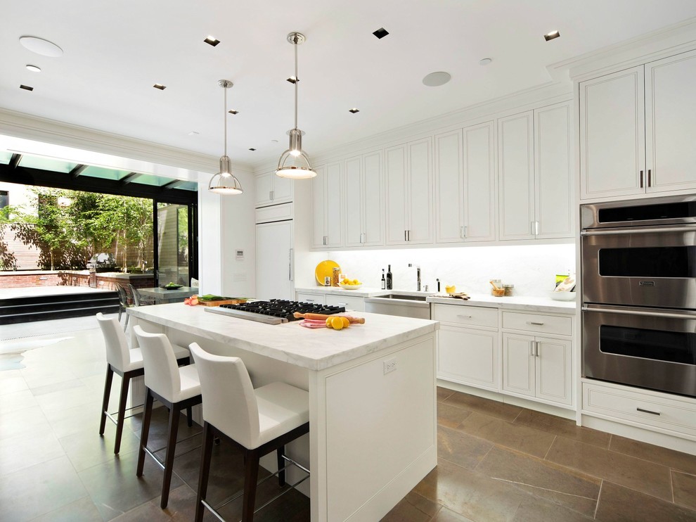 Photo of a transitional galley kitchen in New York with white cabinets, white splashback, stainless steel appliances and with island.