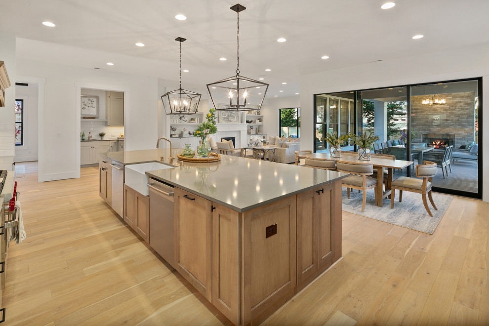 This is an example of a large country l-shaped eat-in kitchen in Seattle with a farmhouse sink, recessed-panel cabinets, grey cabinets, quartz benchtops, white splashback, stainless steel appliances, light hardwood floors, with island, beige floor and grey benchtop.