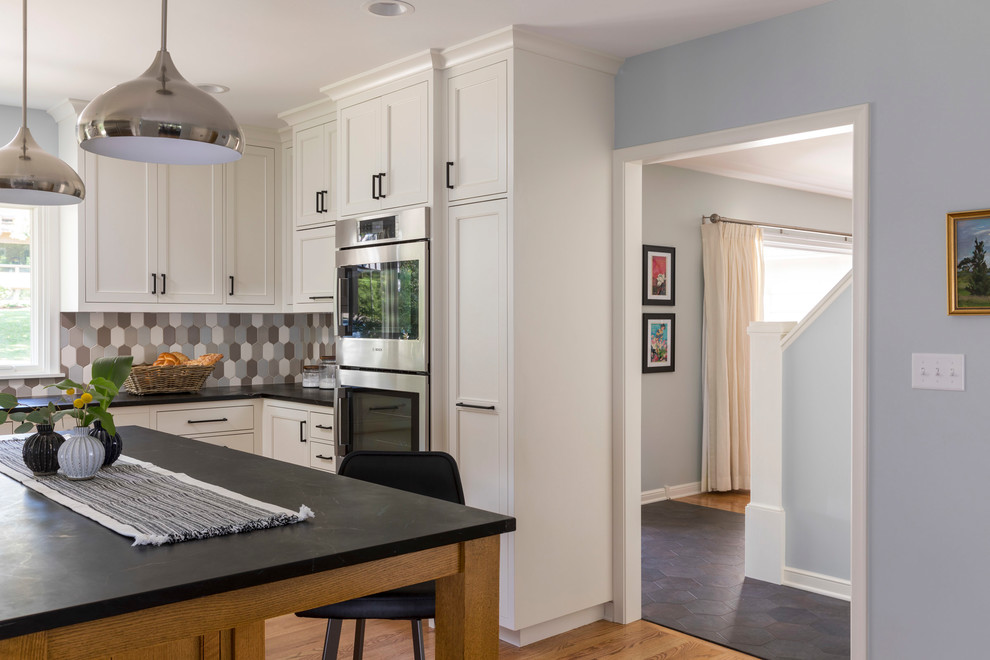 Mid-sized transitional u-shaped medium tone wood floor and brown floor kitchen photo in Minneapolis with an undermount sink, recessed-panel cabinets, white cabinets, granite countertops, multicolored backsplash, ceramic backsplash, stainless steel appliances and an island