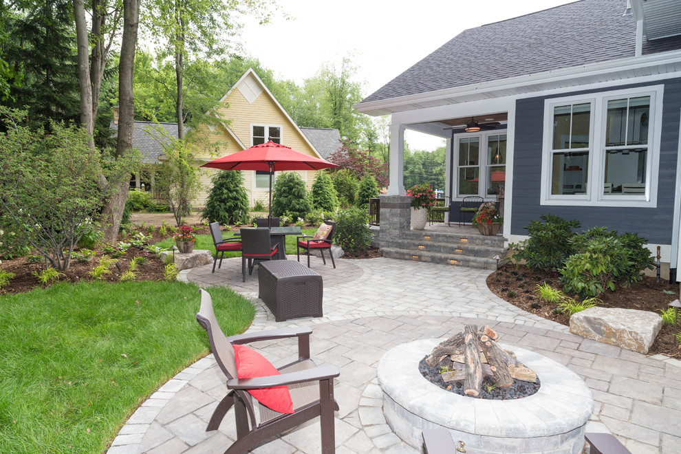 This is an example of a large traditional backyard patio in Grand Rapids with a fire feature, natural stone pavers and no cover.