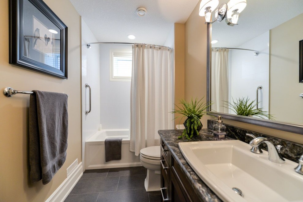 Transitional bathroom in Calgary with shaker cabinets, dark wood cabinets, a shower/bathtub combo, a two-piece toilet, brown walls, a drop-in sink and granite benchtops.