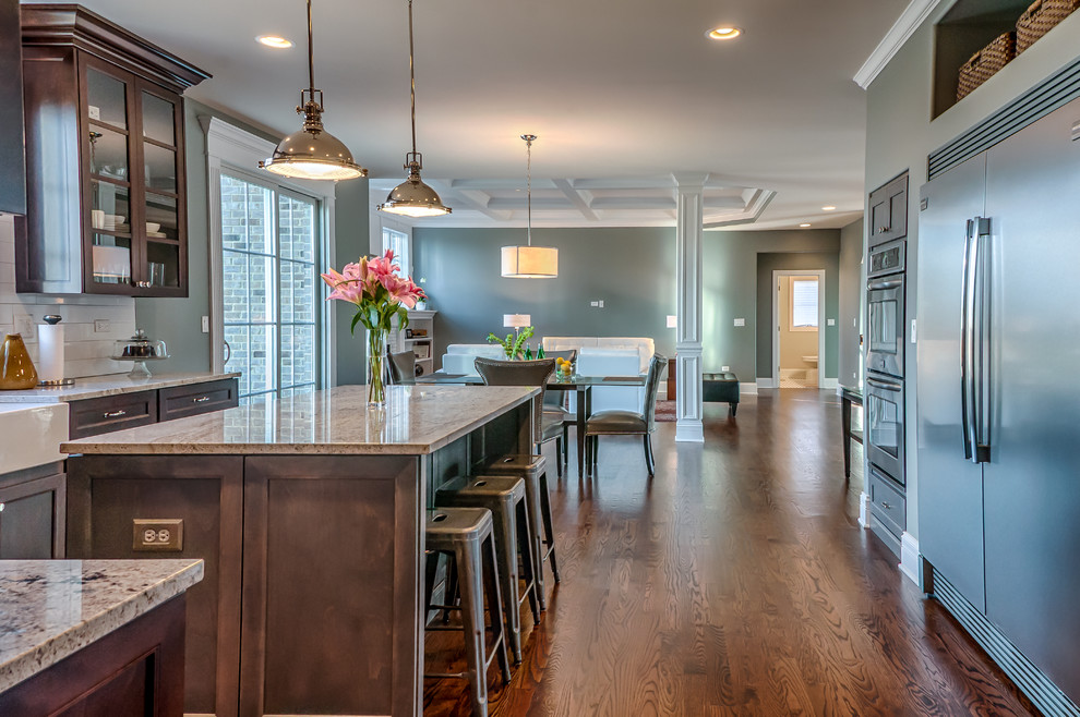 Example of a transitional l-shaped medium tone wood floor eat-in kitchen design in Chicago with a farmhouse sink, shaker cabinets, gray cabinets, granite countertops, yellow backsplash, ceramic backsplash, stainless steel appliances, gray walls and an island