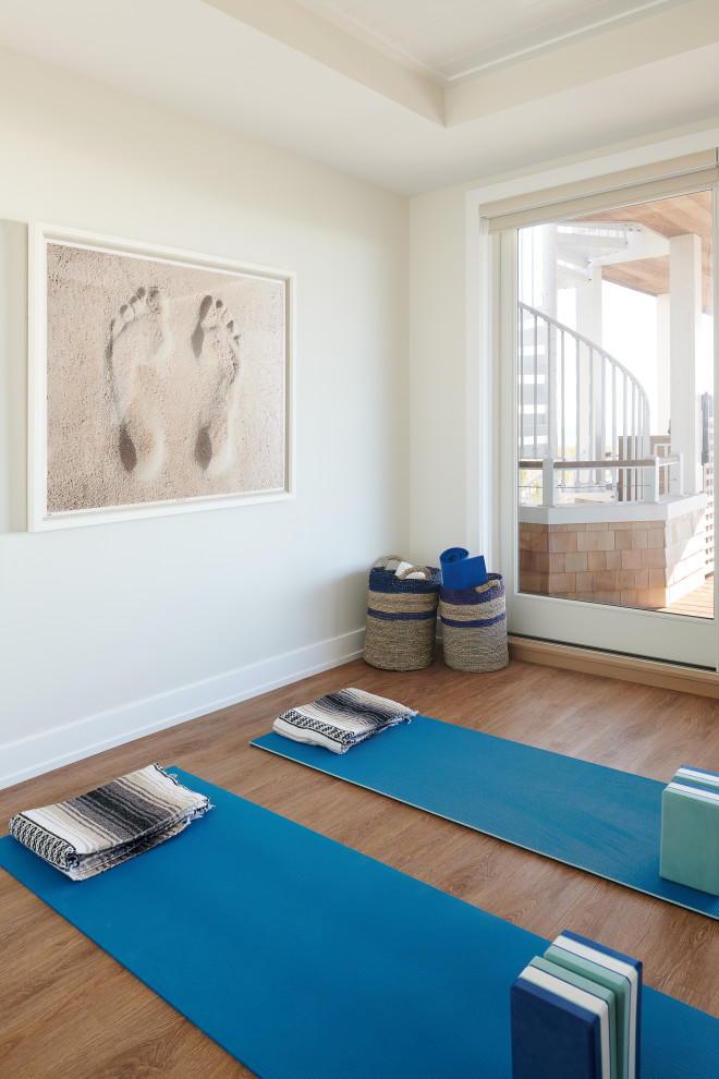 This is an example of a mid-sized beach style home yoga studio in New York with white walls, laminate floors and brown floor.
