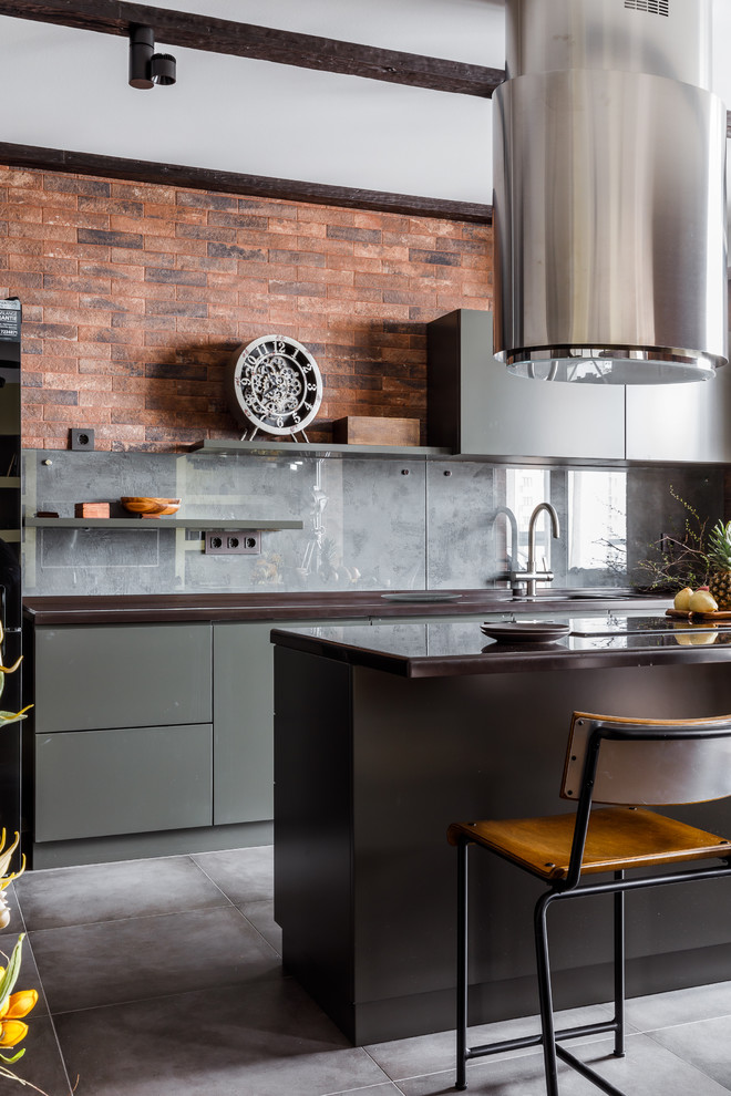 Mid-sized industrial galley open plan kitchen in Other with flat-panel cabinets, grey cabinets, solid surface benchtops, grey splashback, glass sheet splashback, porcelain floors, with island, grey floor and black benchtop.