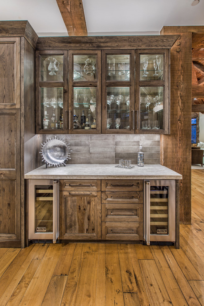 Inspiration for a mid-sized country single-wall wet bar in Denver with glass-front cabinets, distressed cabinets, concrete benchtops, grey splashback, cement tile splashback, light hardwood floors, no sink and brown floor.