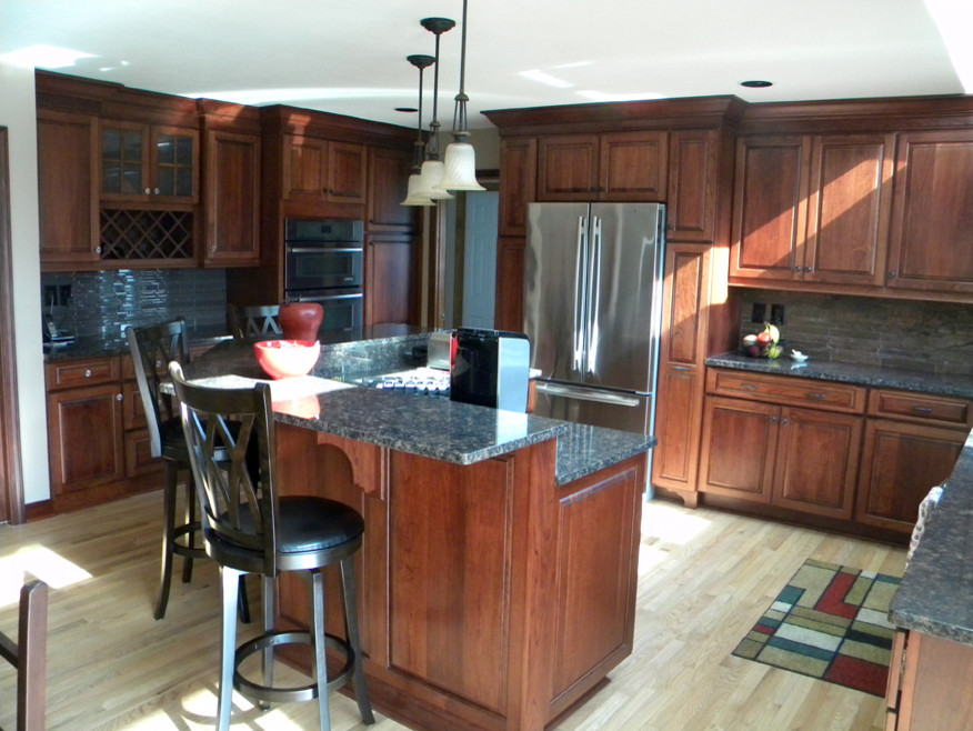 Example of a mid-sized transitional u-shaped light wood floor eat-in kitchen design with an undermount sink, raised-panel cabinets, medium tone wood cabinets, granite countertops, multicolored backsplash, stone tile backsplash, stainless steel appliances and an island
