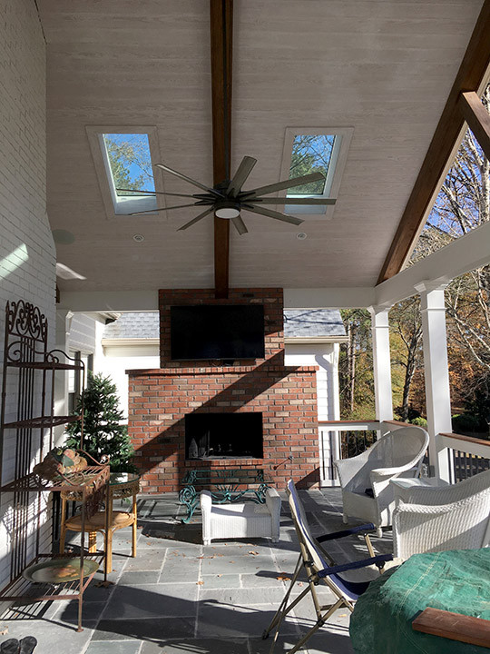 Modelo de terraza campestre grande en patio trasero con chimenea, adoquines de piedra natural, toldo y barandilla de madera