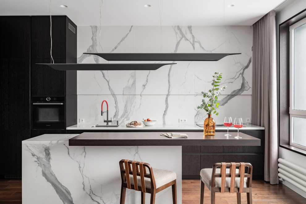Photo of a medium sized contemporary grey and white single-wall open plan kitchen in Moscow with a submerged sink, flat-panel cabinets, black cabinets, white splashback, black appliances, medium hardwood flooring, an island, white worktops, marble worktops and marble splashback.