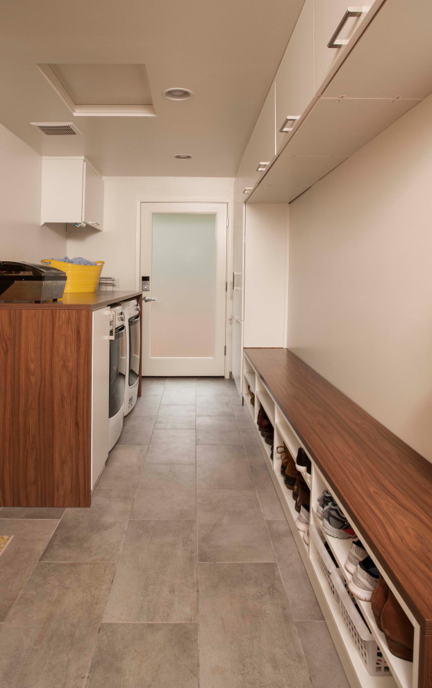 Large midcentury galley dedicated laundry room in Seattle with flat-panel cabinets, white cabinets, wood benchtops, white walls, porcelain floors, an integrated washer and dryer, grey floor and brown benchtop.
