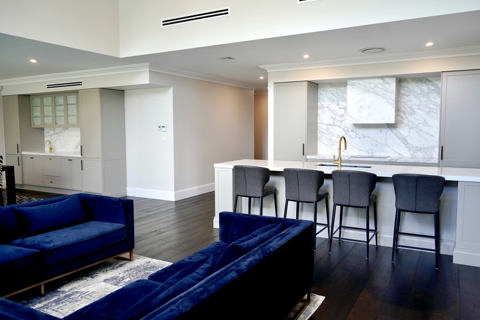 This is an example of a large transitional single-wall open plan kitchen in Sydney with an undermount sink, shaker cabinets, grey cabinets, marble benchtops, white splashback, marble splashback, black appliances, dark hardwood floors, with island, brown floor and white benchtop.