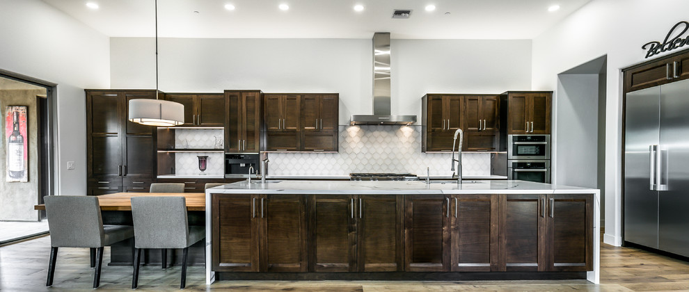 Inspiration for an expansive transitional l-shaped open plan kitchen in Phoenix with an undermount sink, recessed-panel cabinets, dark wood cabinets, quartz benchtops, white splashback, glass tile splashback, stainless steel appliances, light hardwood floors, with island, brown floor and multi-coloured benchtop.