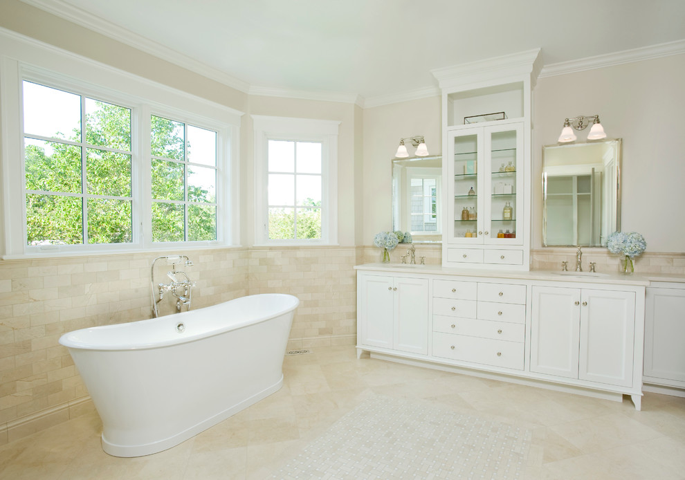 Beach style bathroom in Boston with white cabinets, a freestanding tub, beige tile, an undermount sink, recessed-panel cabinets, subway tile and beige floor.