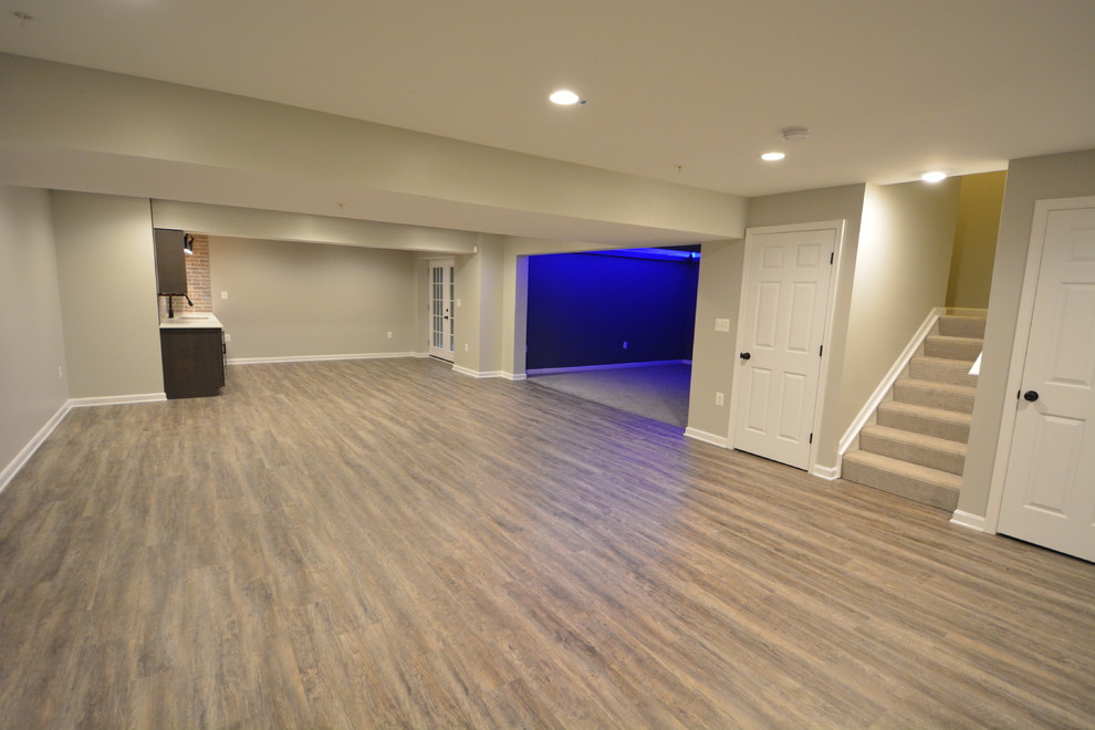 This is an example of a large transitional walk-out basement in Baltimore with beige walls, vinyl floors, no fireplace and brown floor.