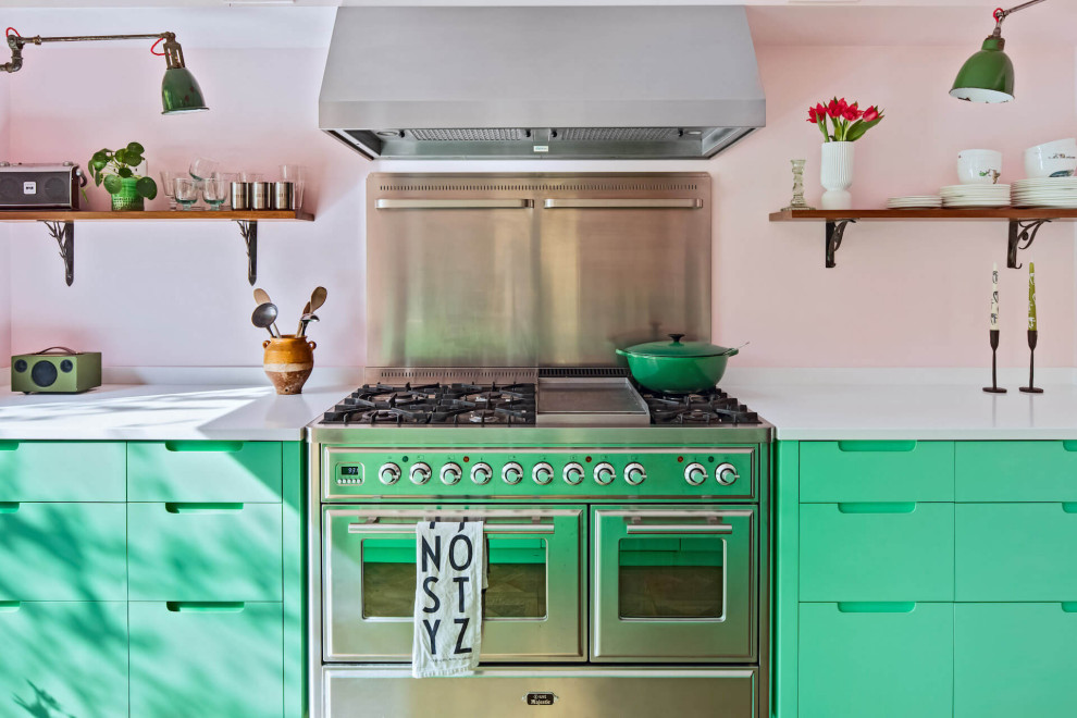 Cette image montre une cuisine américaine linéaire bohème de taille moyenne avec un placard à porte plane, des portes de placards vertess, un plan de travail en surface solide, îlot et un plan de travail blanc.