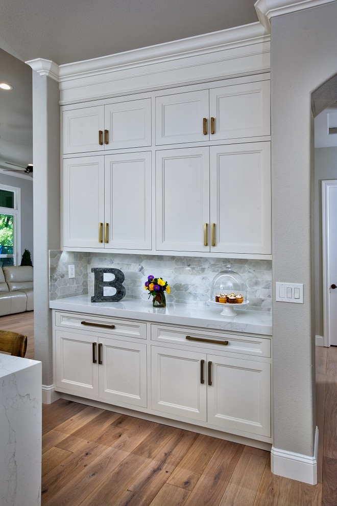 Example of a mid-sized transitional u-shaped light wood floor eat-in kitchen design in Sacramento with a farmhouse sink, white cabinets, gray backsplash, stainless steel appliances, an island and white countertops