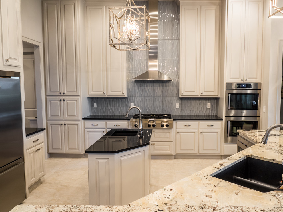 Example of a large transitional u-shaped eat-in kitchen design with an undermount sink, raised-panel cabinets, white cabinets, granite countertops, gray backsplash, ceramic backsplash, stainless steel appliances and two islands