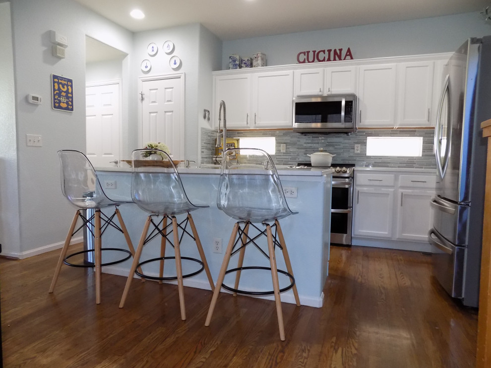 Foto på ett litet funkis vit u-kök, med en undermonterad diskho, luckor med infälld panel, vita skåp, bänkskiva i kvartsit, blått stänkskydd, stänkskydd i glaskakel, rostfria vitvaror, målat trägolv, en köksö och gult golv