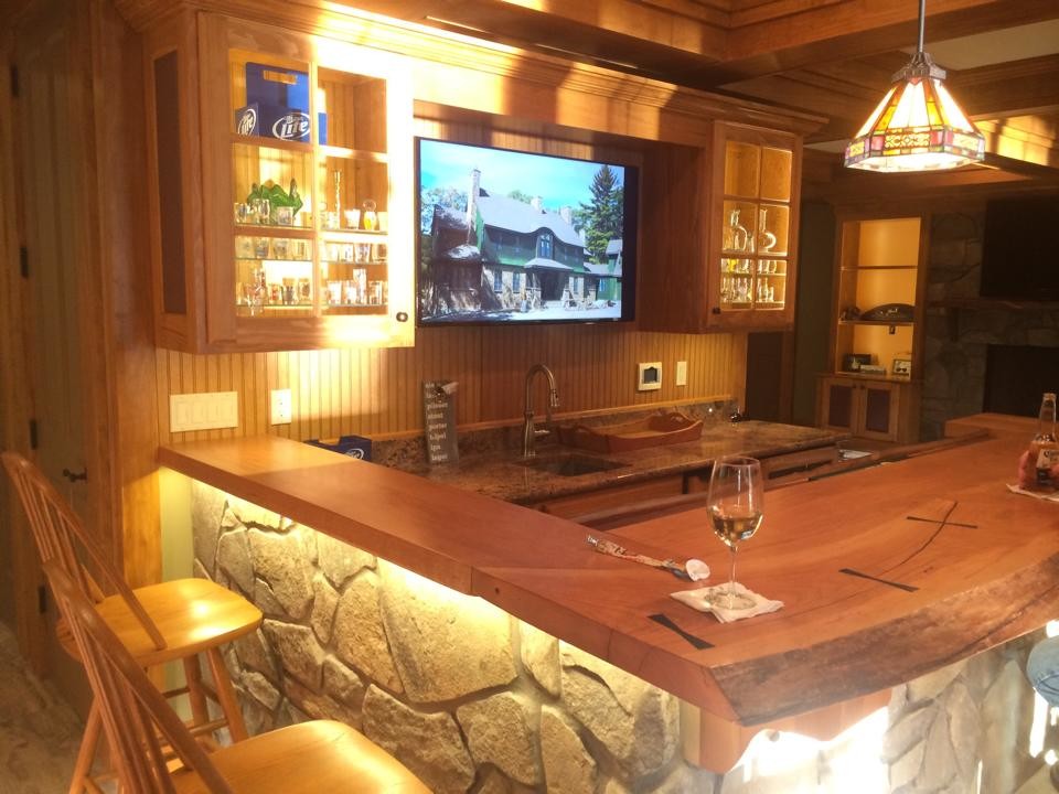 This is an example of a mid-sized country l-shaped seated home bar in Other with an undermount sink, glass-front cabinets, light wood cabinets, granite benchtops and timber splashback.