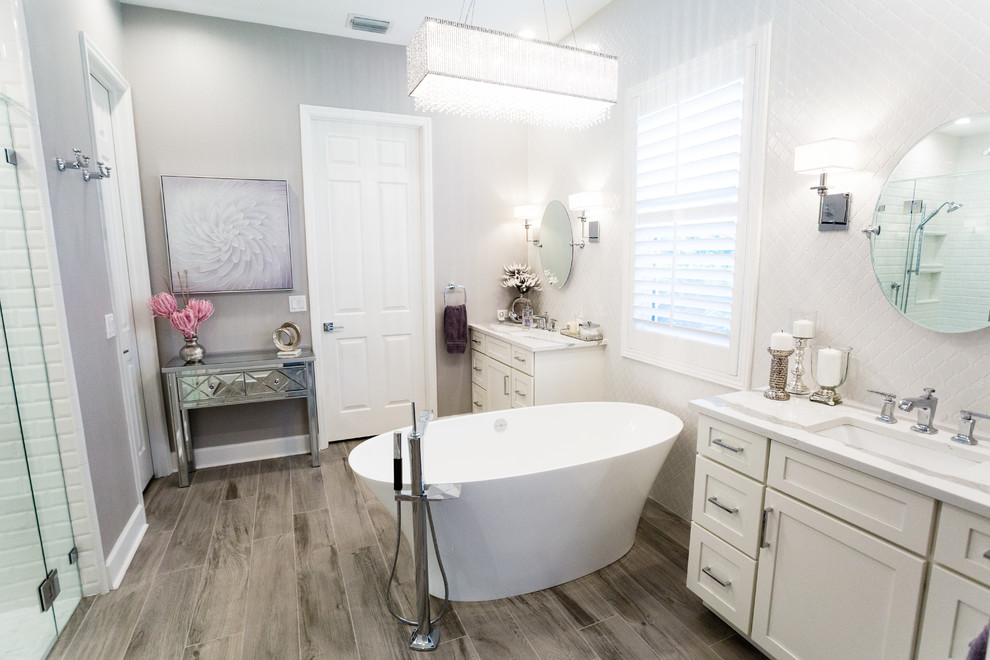 Inspiration for a mid-sized transitional master bathroom in Tampa with shaker cabinets, white cabinets, a freestanding tub, an alcove shower, a one-piece toilet, white tile, porcelain tile, grey walls, porcelain floors, an undermount sink, glass benchtops, brown floor, a hinged shower door and white benchtops.