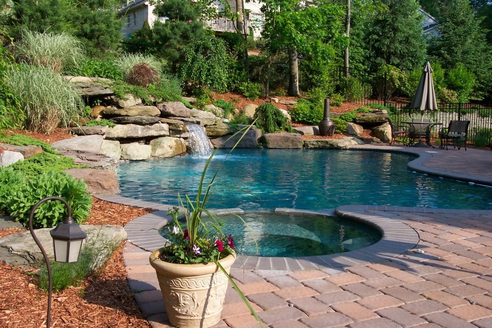 Design ideas for an expansive country backyard custom-shaped natural pool in New York with a water feature and brick pavers.