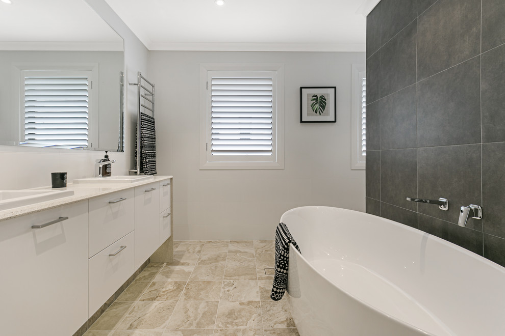 This is an example of a mid-sized contemporary master bathroom in Sydney with white cabinets, a freestanding tub, black and white tile, ceramic tile, beige walls, ceramic floors, a wall-mount sink, engineered quartz benchtops, beige floor, flat-panel cabinets, an open shower, a one-piece toilet, a hinged shower door and white benchtops.