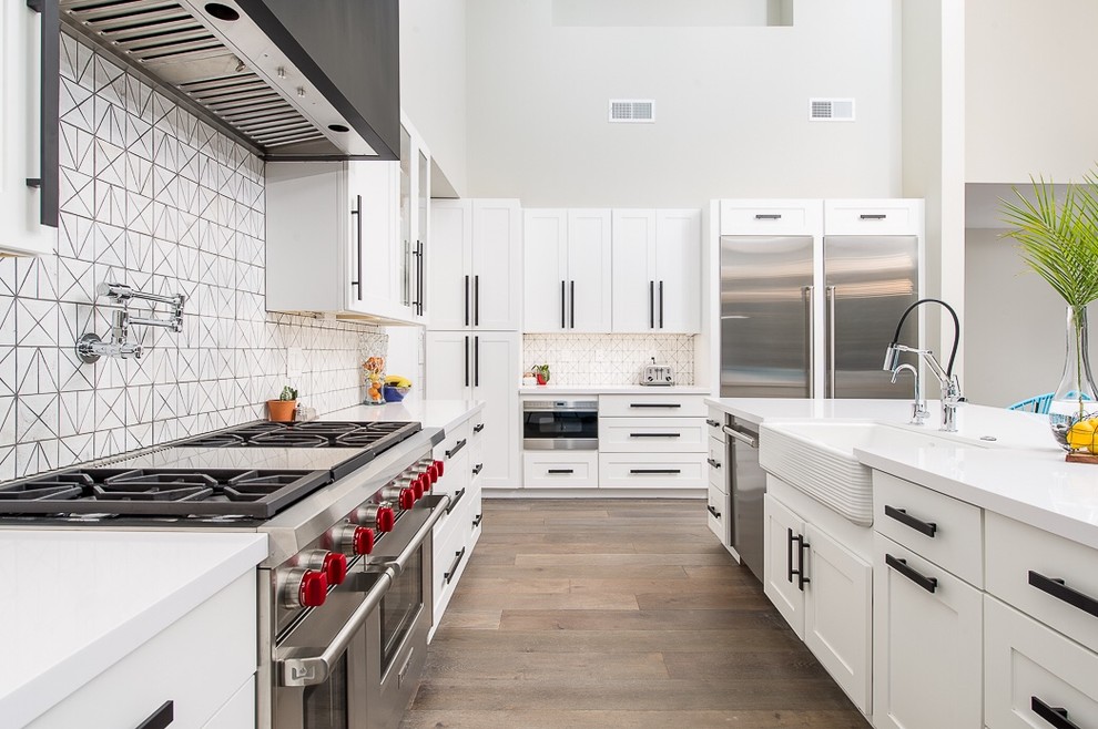 Inspiration for a large transitional u-shaped eat-in kitchen in Phoenix with a farmhouse sink, white cabinets, white splashback, stainless steel appliances, light hardwood floors, with island, shaker cabinets, solid surface benchtops and ceramic splashback.