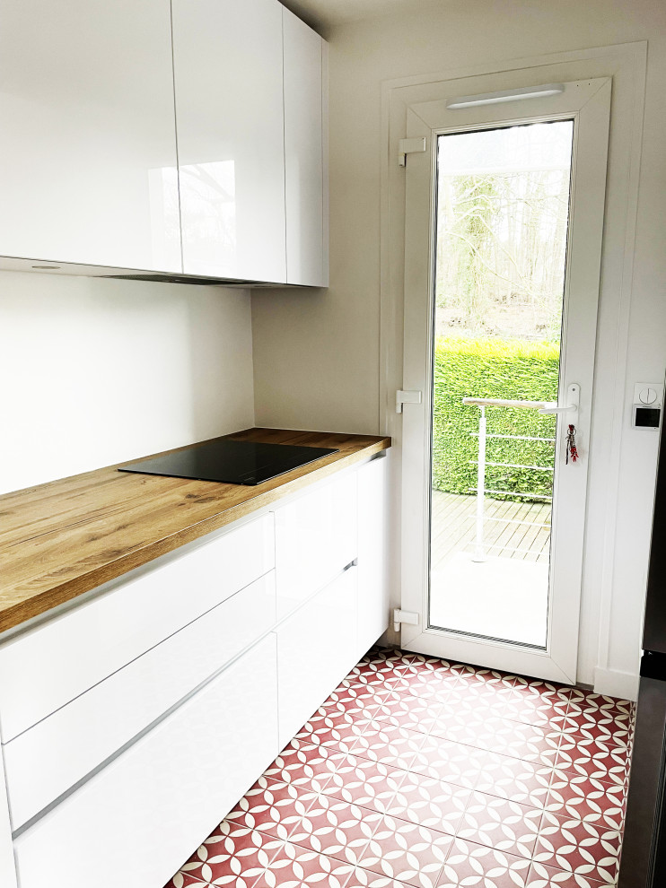 Inspiration for a mid-sized midcentury galley separate kitchen in Paris with an undermount sink, flat-panel cabinets, white cabinets, wood benchtops, white splashback, glass sheet splashback, black appliances, ceramic floors, no island, red floor and brown benchtop.
