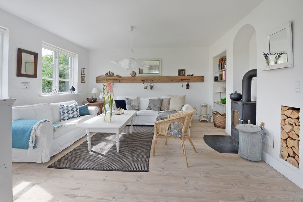 Photo of a scandinavian living room in Odense with white walls, light hardwood floors, a wood stove, a metal fireplace surround and beige floor.