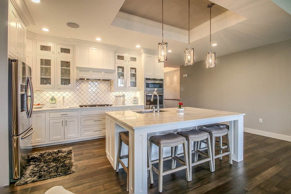 Eat-in kitchen - transitional l-shaped medium tone wood floor and brown floor eat-in kitchen idea with an undermount sink, recessed-panel cabinets, white cabinets, white backsplash, ceramic backsplash, stainless steel appliances and an island