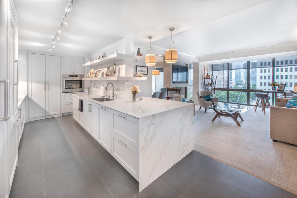 Photo of a contemporary l-shaped open plan kitchen in Atlanta with a single-bowl sink, recessed-panel cabinets, white cabinets, grey splashback, stainless steel appliances, with island, grey floor and white benchtop.