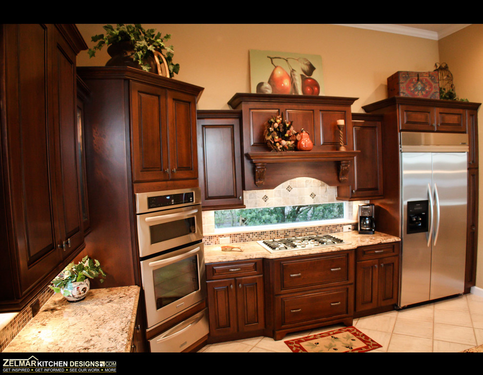 Photo of a large traditional l-shaped eat-in kitchen in Orlando with an undermount sink, raised-panel cabinets, brown cabinets, granite benchtops, beige splashback, stone tile splashback and with island.