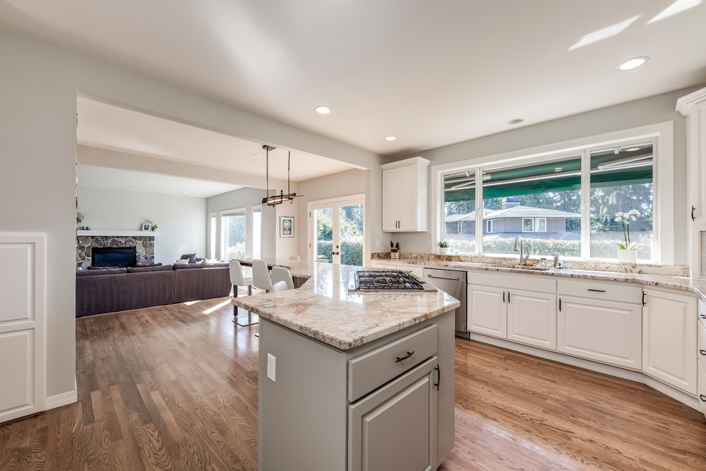 Photo of an expansive transitional l-shaped open plan kitchen in Seattle with a double-bowl sink, raised-panel cabinets, white cabinets, quartzite benchtops, white splashback, stone slab splashback, stainless steel appliances, medium hardwood floors, with island, brown floor and beige benchtop.