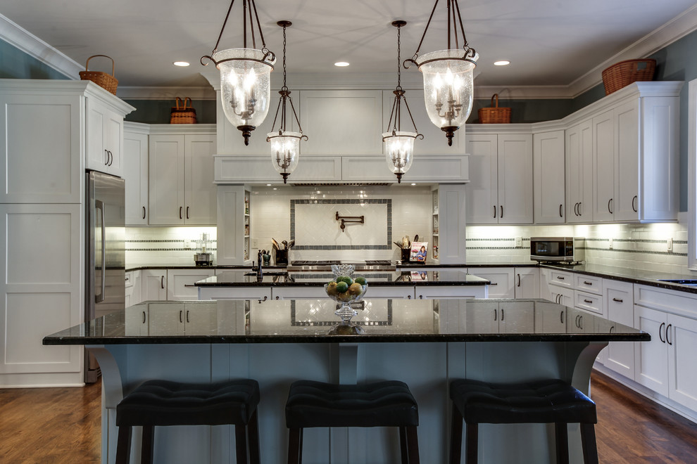 Inspiration for a mid-sized transitional u-shaped eat-in kitchen in Chicago with an undermount sink, shaker cabinets, white cabinets, laminate benchtops, white splashback, subway tile splashback, stainless steel appliances, dark hardwood floors, multiple islands and brown floor.