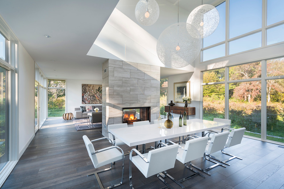 Photo of a large contemporary open plan dining in Boston with white walls, dark hardwood floors, a two-sided fireplace and a tile fireplace surround.
