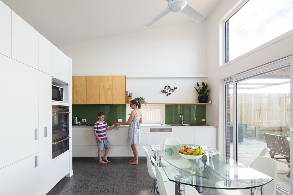 This is an example of a contemporary eat-in kitchen in Canberra - Queanbeyan with green splashback, glass sheet splashback and concrete floors.