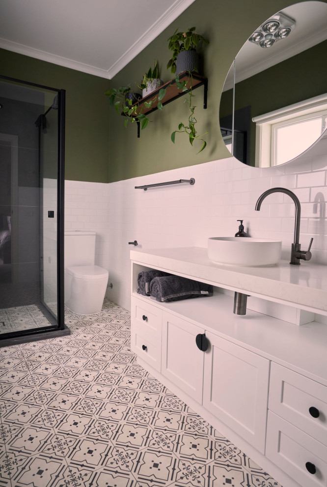 На фото: ванная комната среднего размера в современном стиле с фасадами с утопленной филенкой, белыми фасадами, угловым душем, унитазом-моноблоком, белой плиткой, керамической плиткой, зелеными стенами, полом из цементной плитки, настольной раковиной, столешницей из искусственного кварца, душем с распашными дверями, белой столешницей, нишей, тумбой под одну раковину и встроенной тумбой