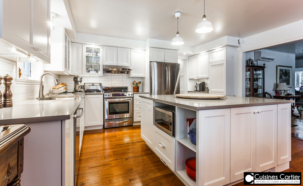 Example of a large transitional medium tone wood floor eat-in kitchen design in Montreal with a double-bowl sink, shaker cabinets, white cabinets, quartzite countertops, white backsplash, ceramic backsplash, stainless steel appliances and an island