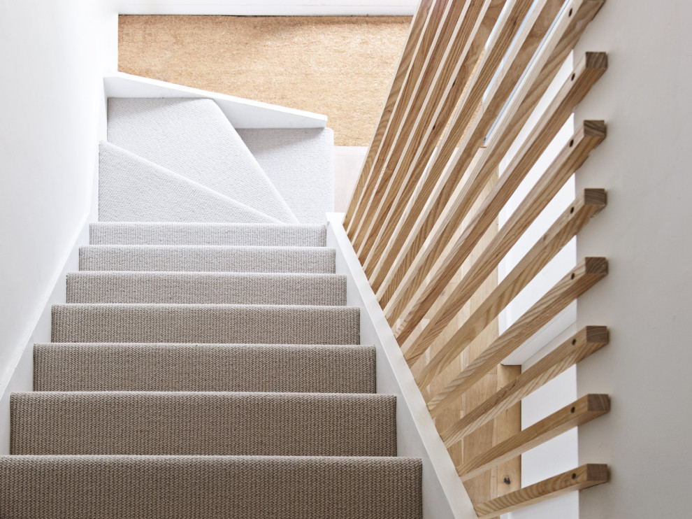 Design ideas for a small modern carpeted straight staircase in London with carpet risers and wood railing.