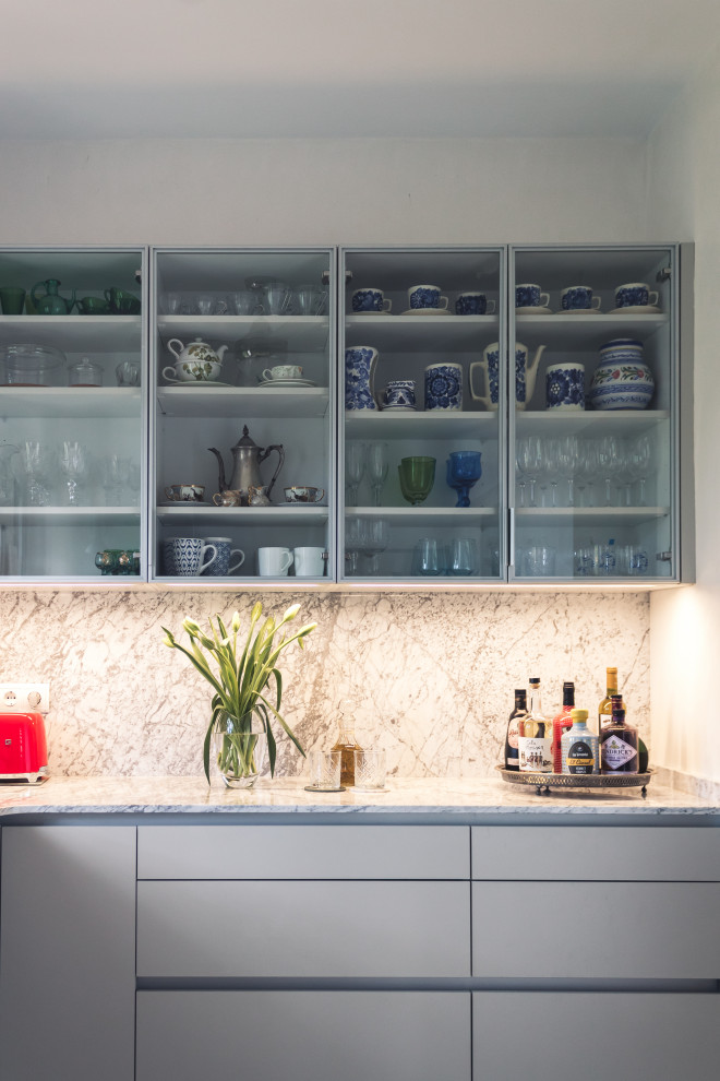 Photo of a large classic u-shaped dry bar in Other with a submerged sink, glass-front cabinets, grey cabinets, marble worktops, white splashback, marble splashback, ceramic flooring, beige floors and white worktops.